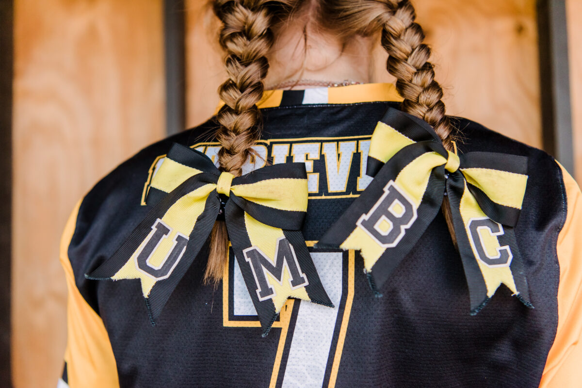 View of softball player's braided hair from behind with ribbons spelling "UMBC"