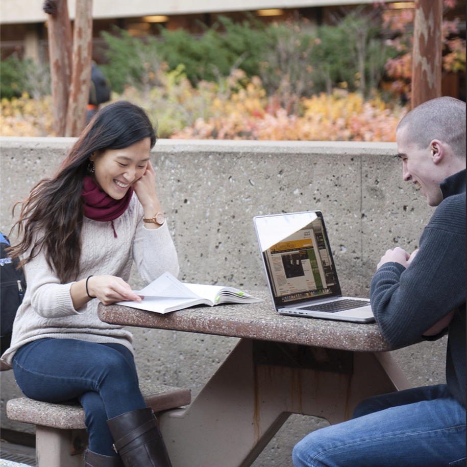 A young Asian woman and young white man sitting across from each other while reading and studying.