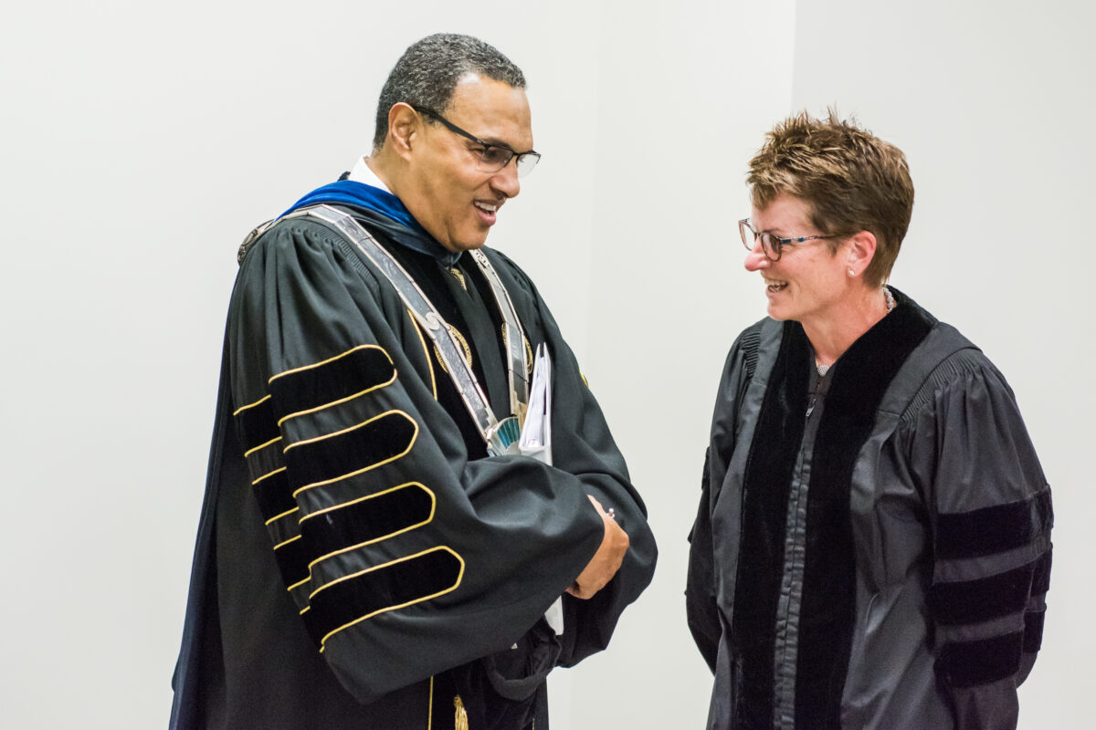 Freeman Hrabowski and Erin O'Shea, smiling and in graduation robes, in a white-walled space