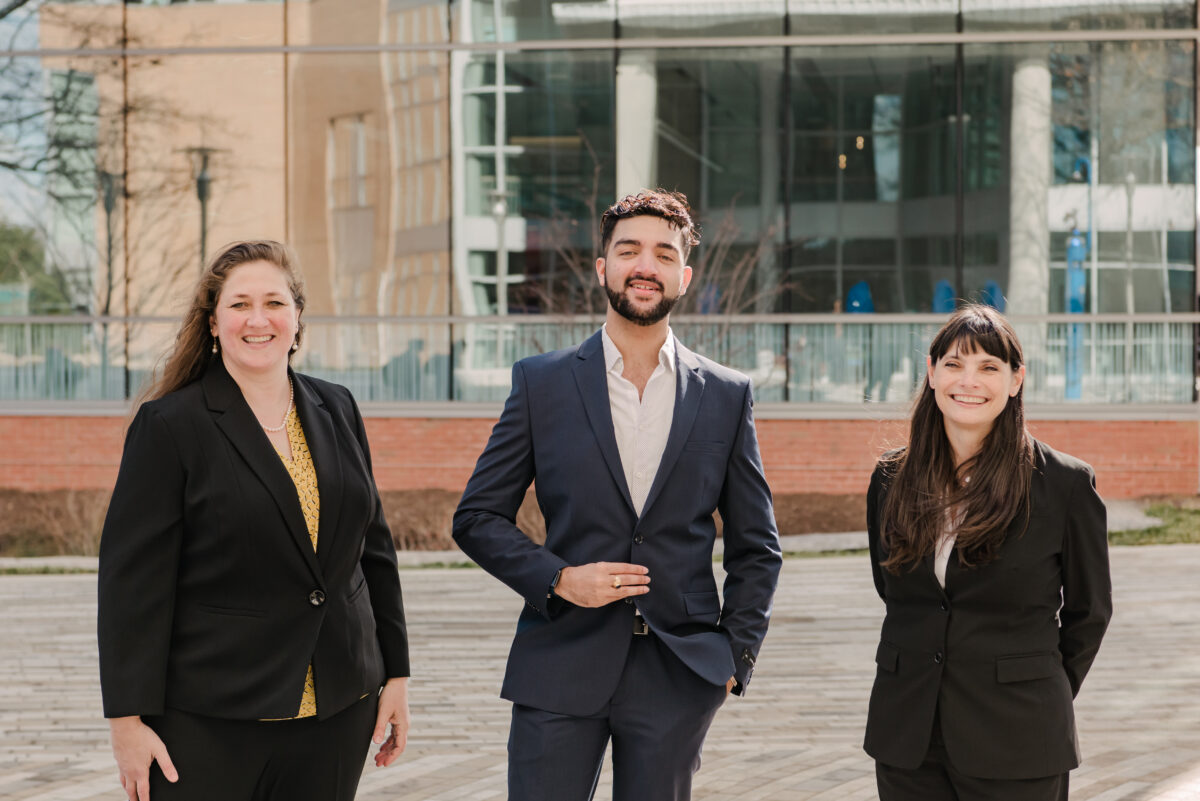 Three adults wearing suits stand next to each other in front of a building.