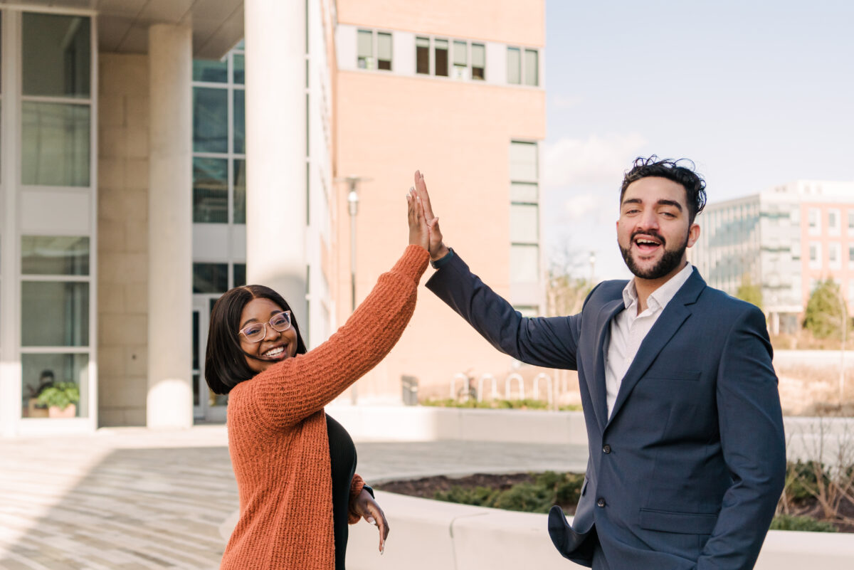 Two people high-fiving each other while standing in front of a brick building.