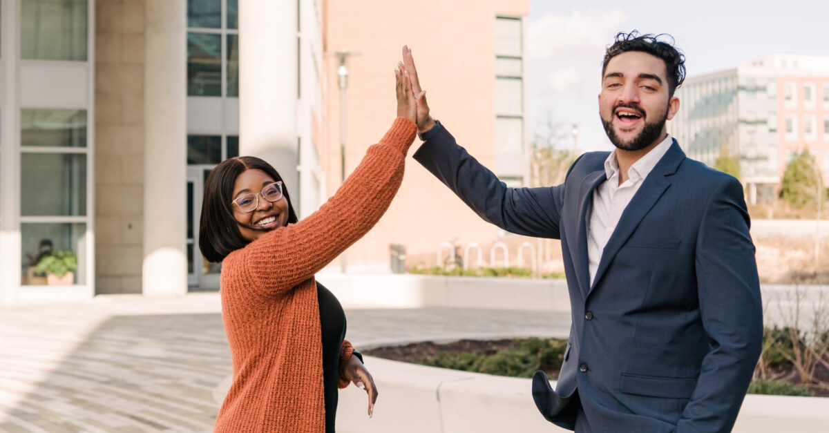 Two people high-fiving each other while standing in front of a brick building.