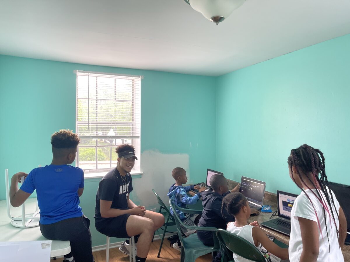 young children work at computers in a brightly painted room while UMBC student Micah Thorpe supervises.