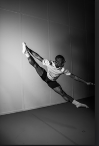 A black and white photo of a dancer in mid air with legs outstretched at UMBC.