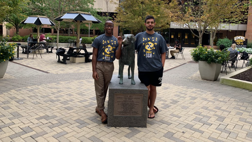 Two adults wearing black t-shirts, stand with a bronze sculpture of a dog at UMBC.