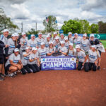 Softball players and coaches huddled around "America East Champions" banner