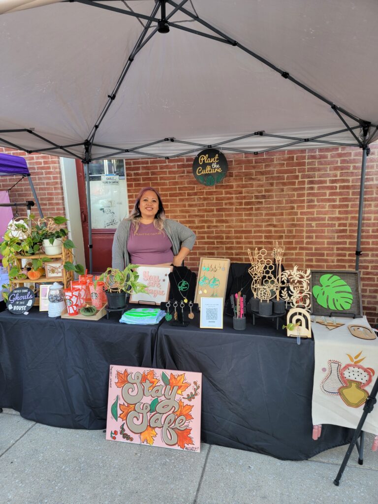 Woman smiling standing at a table with plant-themed art and jewelry