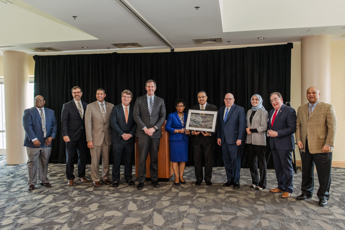 11 people in business attire stand with a framed photograph