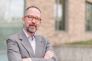Timothy Nohe, a white man with graying hair and a beard, wearing glasses and a gray jacket