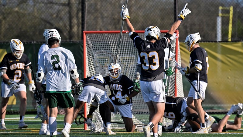 UMBC is well-known for its men's lacrosse teams. Pictured here is a group of young men in their lacrosse uniforms, after a game. One young man wearing jersey number 33 has his arms up in celebration, while others around him are in motion, all moving toward the goal.