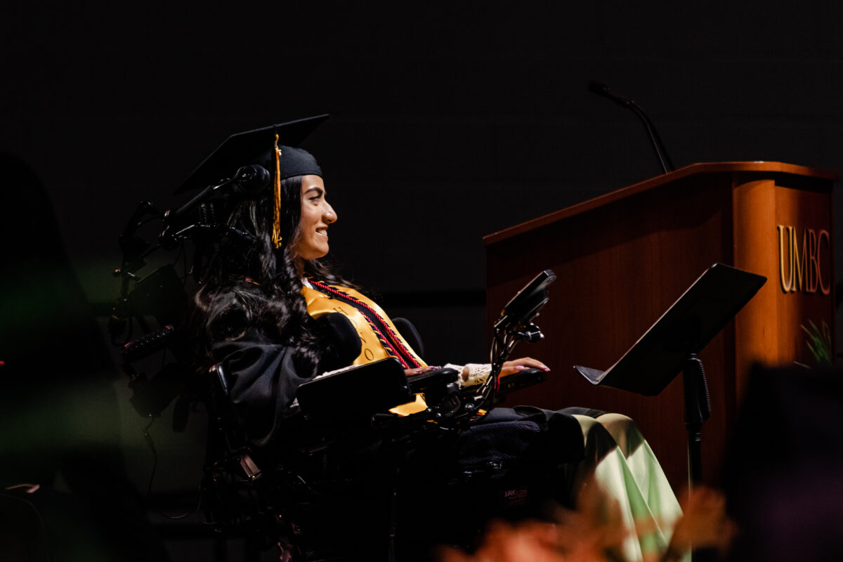 Woman in a wheelchair and graduation regalia adressing crowd