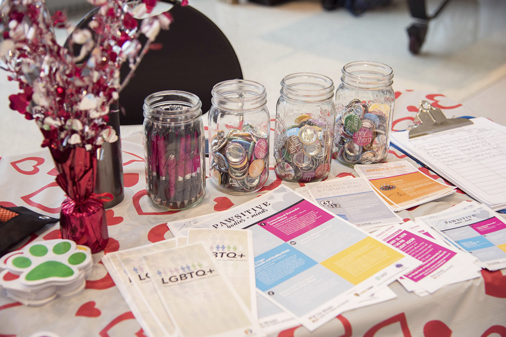 An events table with colorful decor displays UMBC paw stickers, jars full of buttons, and pamphlets featuring LGBTQ+ information and other support groups.