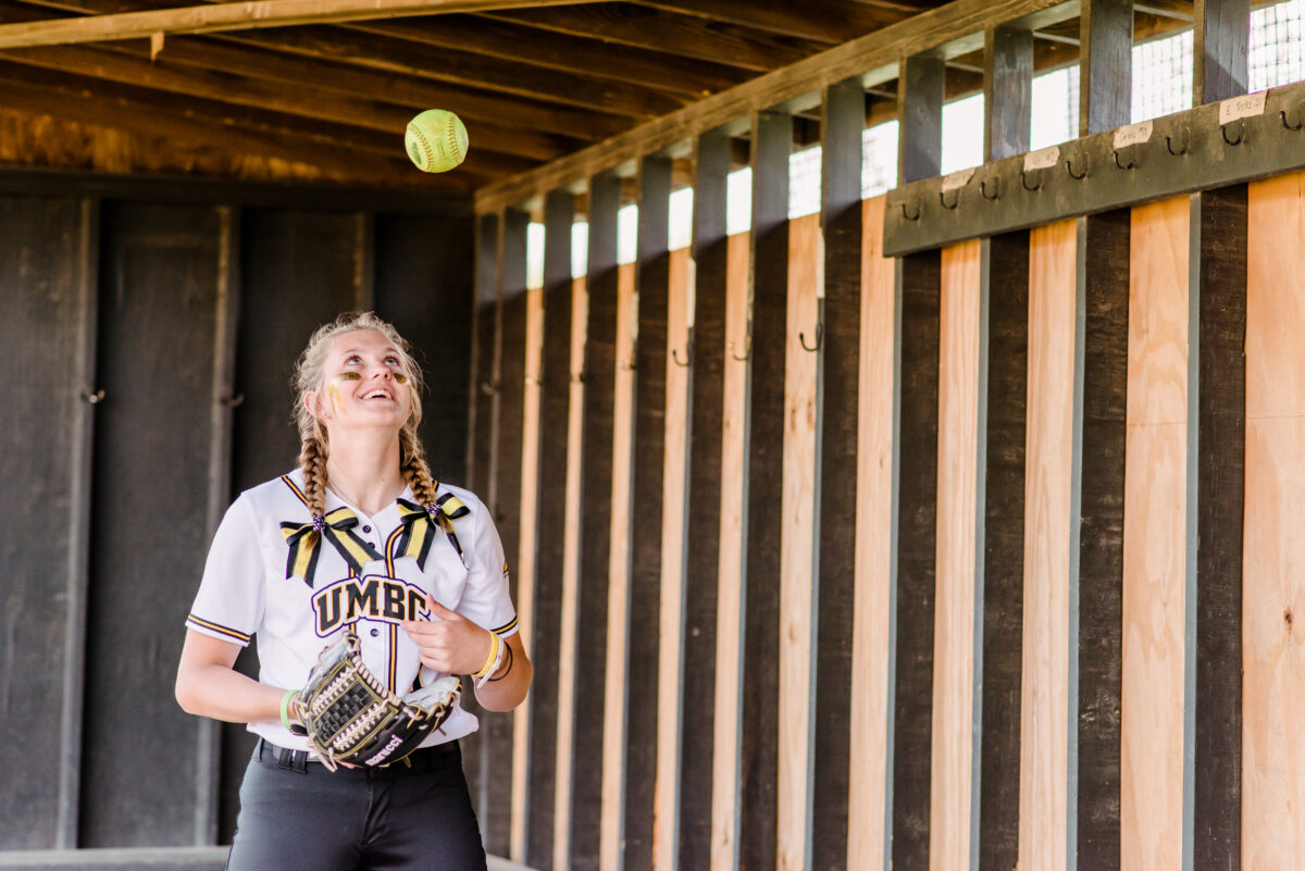 Softball player in black and gold throw a ball midair