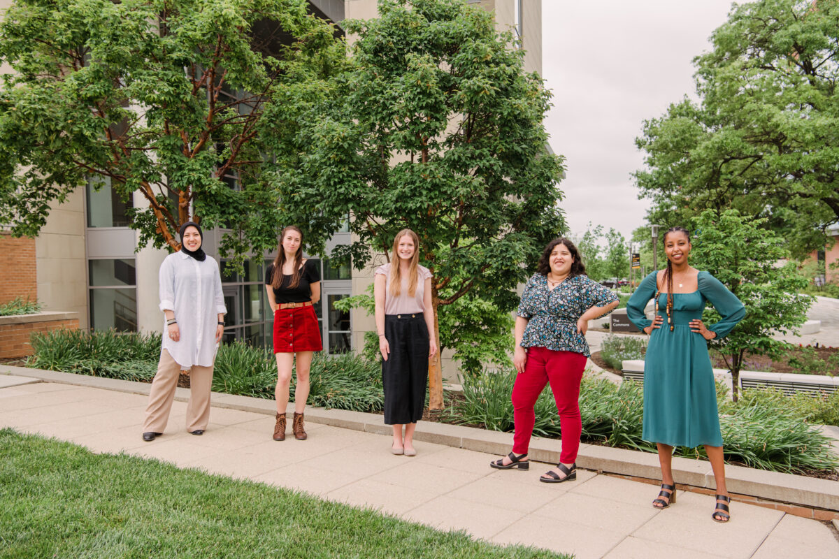 Five adults stand outside next to each other on a pathway. Fulbright.