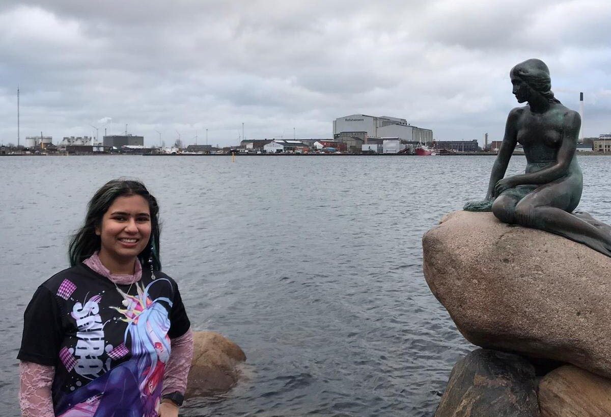 A person stands by a body of water next to a bronze statue of a mermaid.