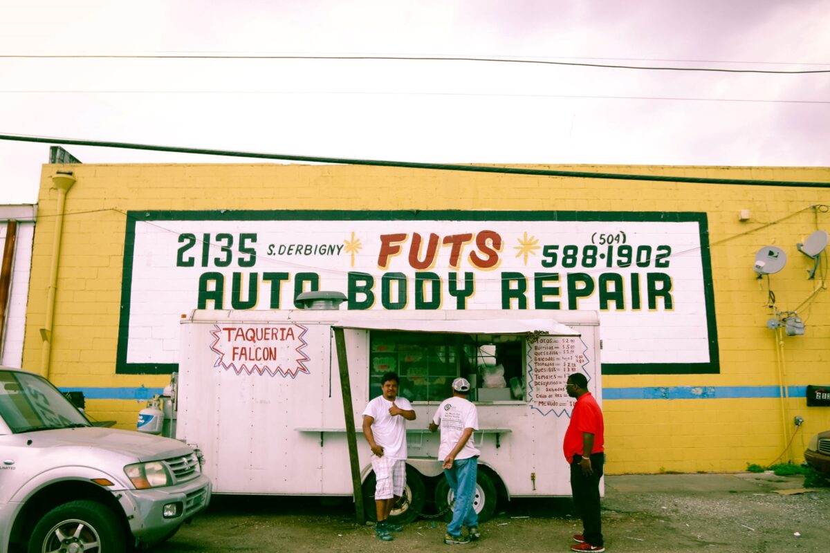 Three people are standing by a food truck with a large yellow cement wall. Photo by Fernando López. New Orleans.