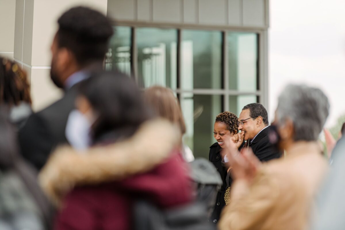 Two adults in black jackets (past and future UMBC leaders) are in a crowd. They are in focus while others are blurred.