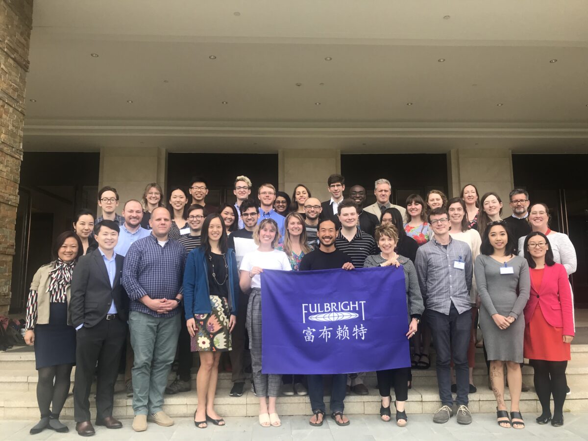 A large group of people in business casual clothing stand close together and hold a purple banner with the words Fulbright written in English and Chinese.
