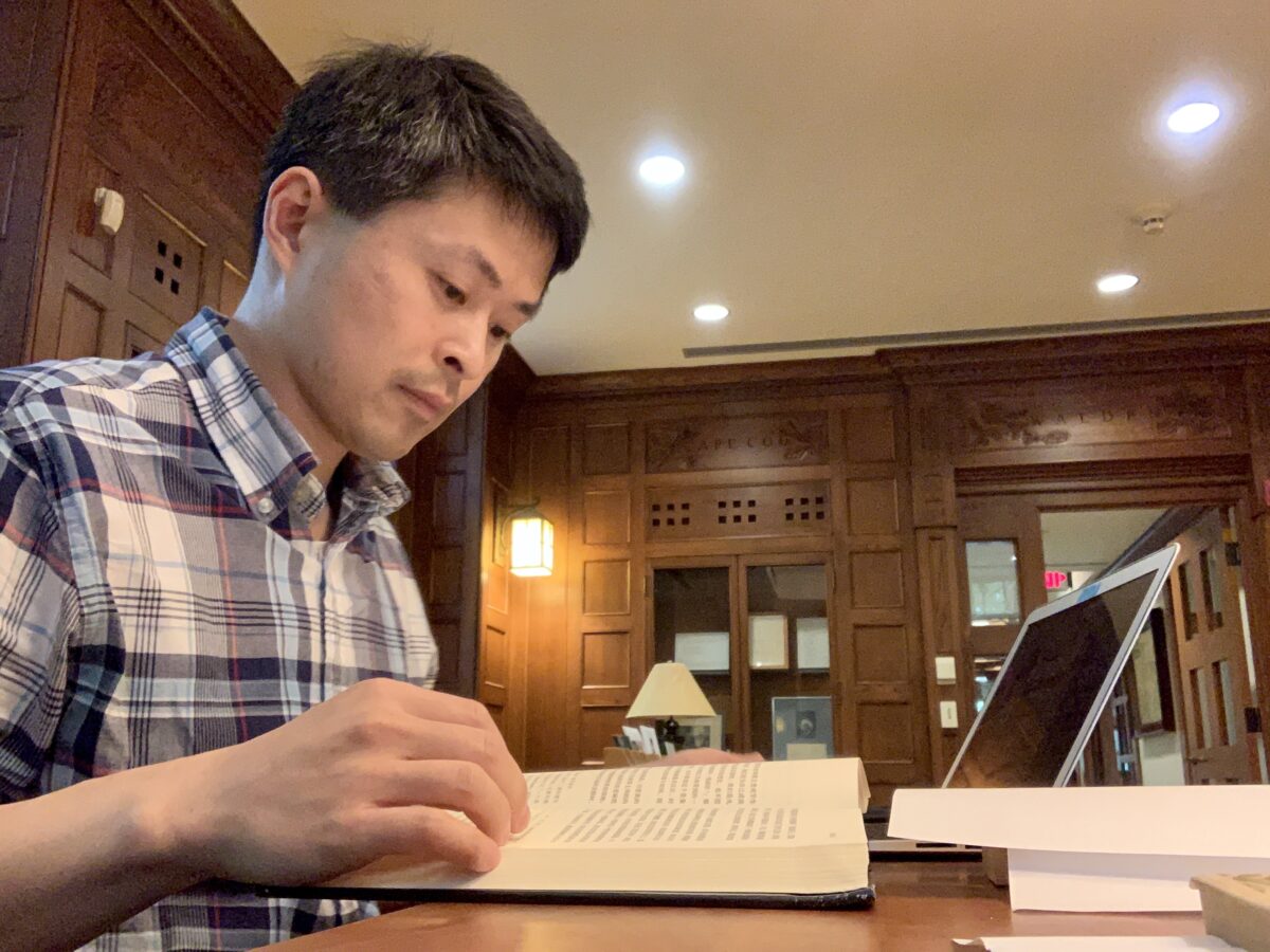 A person sitting at a table looking through a book in a room with wooden shelves. Yangtzi River
    