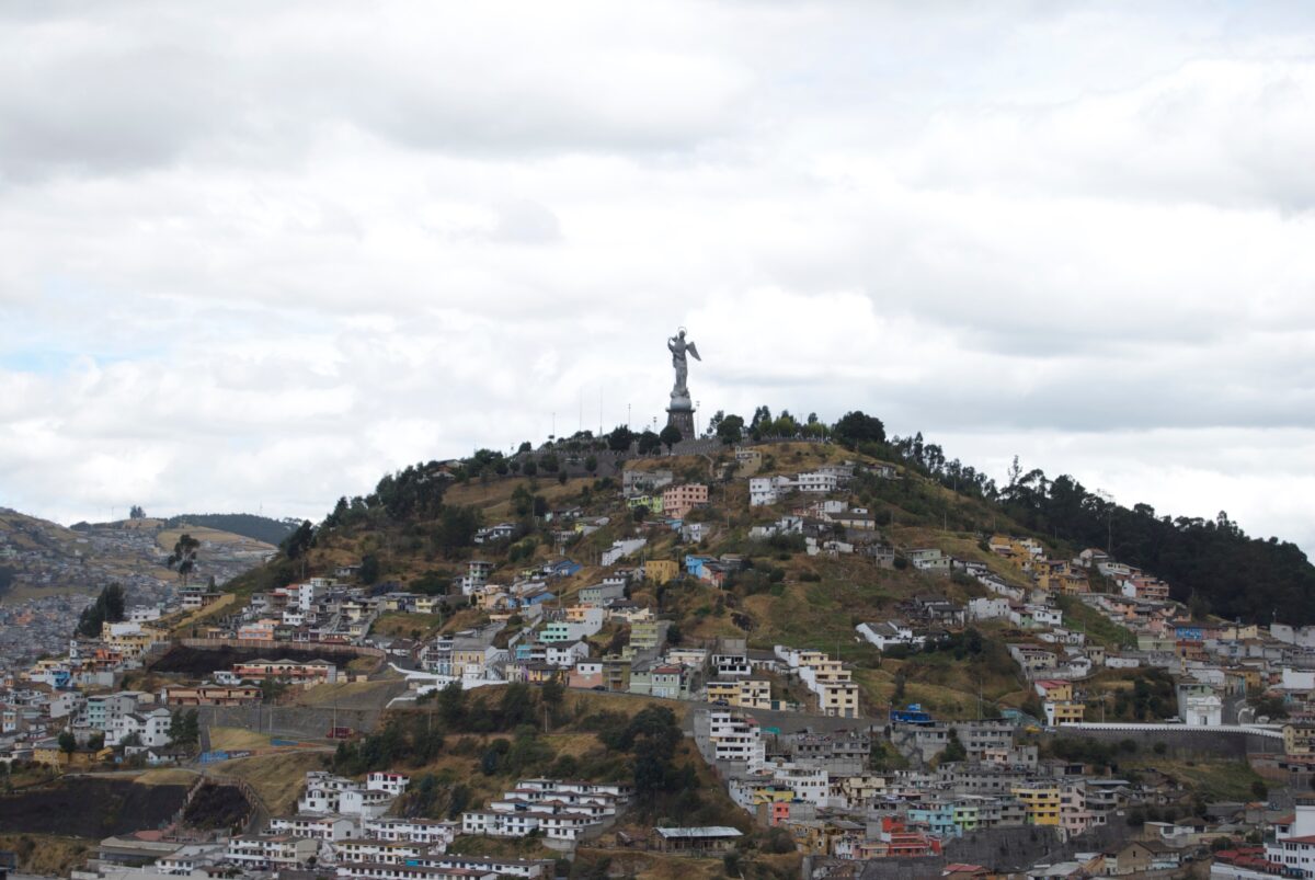 A large aluminum statue of the Virgen del Panecillo stands on top of a hill overlooking multicolored homes in Quito, Ecuador.