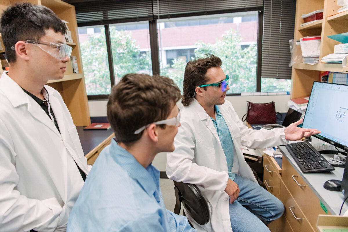 two seated researchers, one standing, discussing a figure on a computer screen