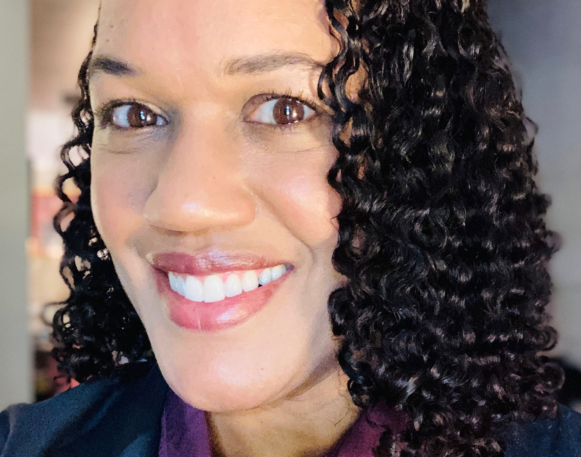 A Black woman with dark curly hair is smiling with her face close to the camera.