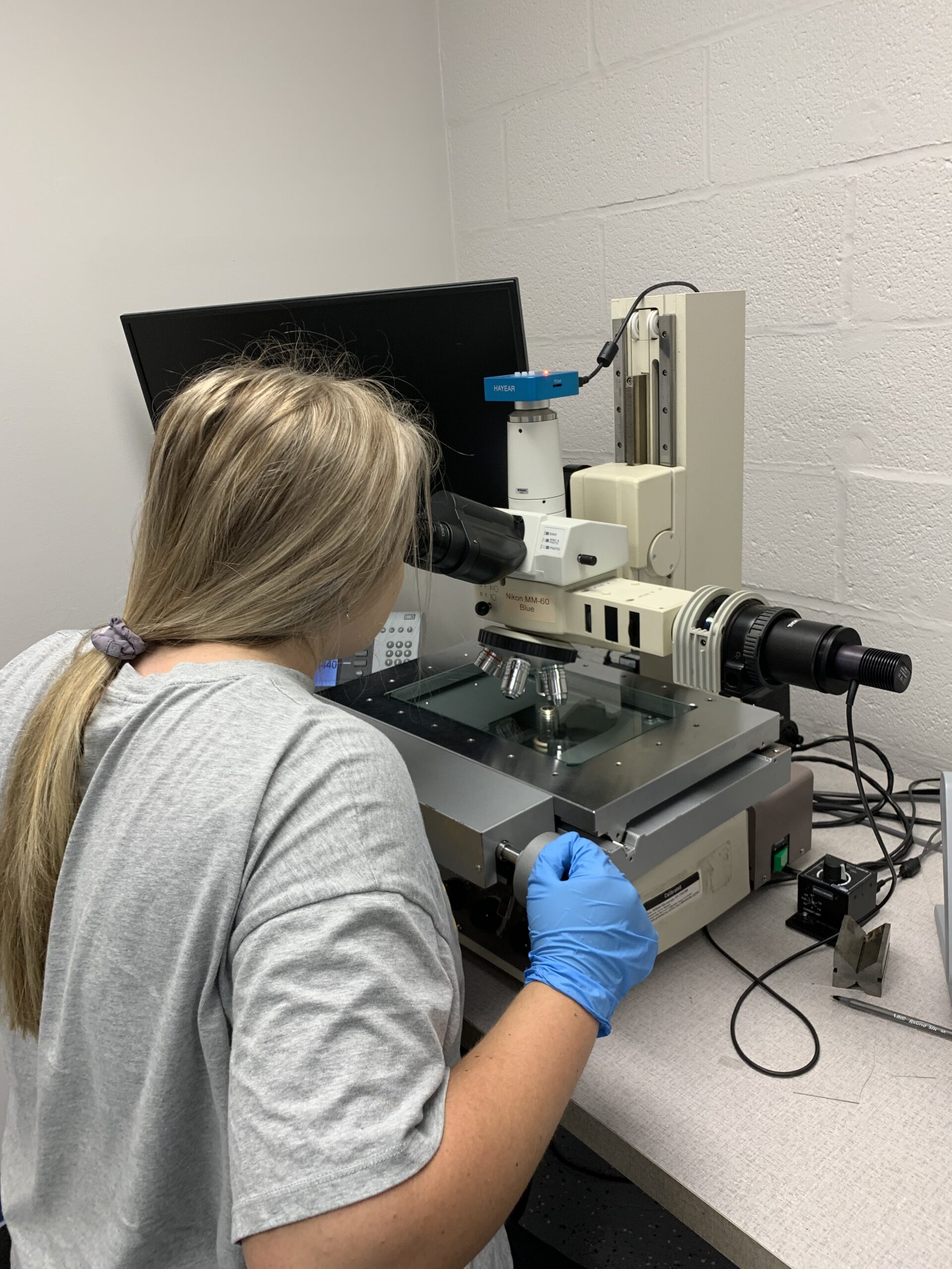 A woman with a ponytail looks into a microscope