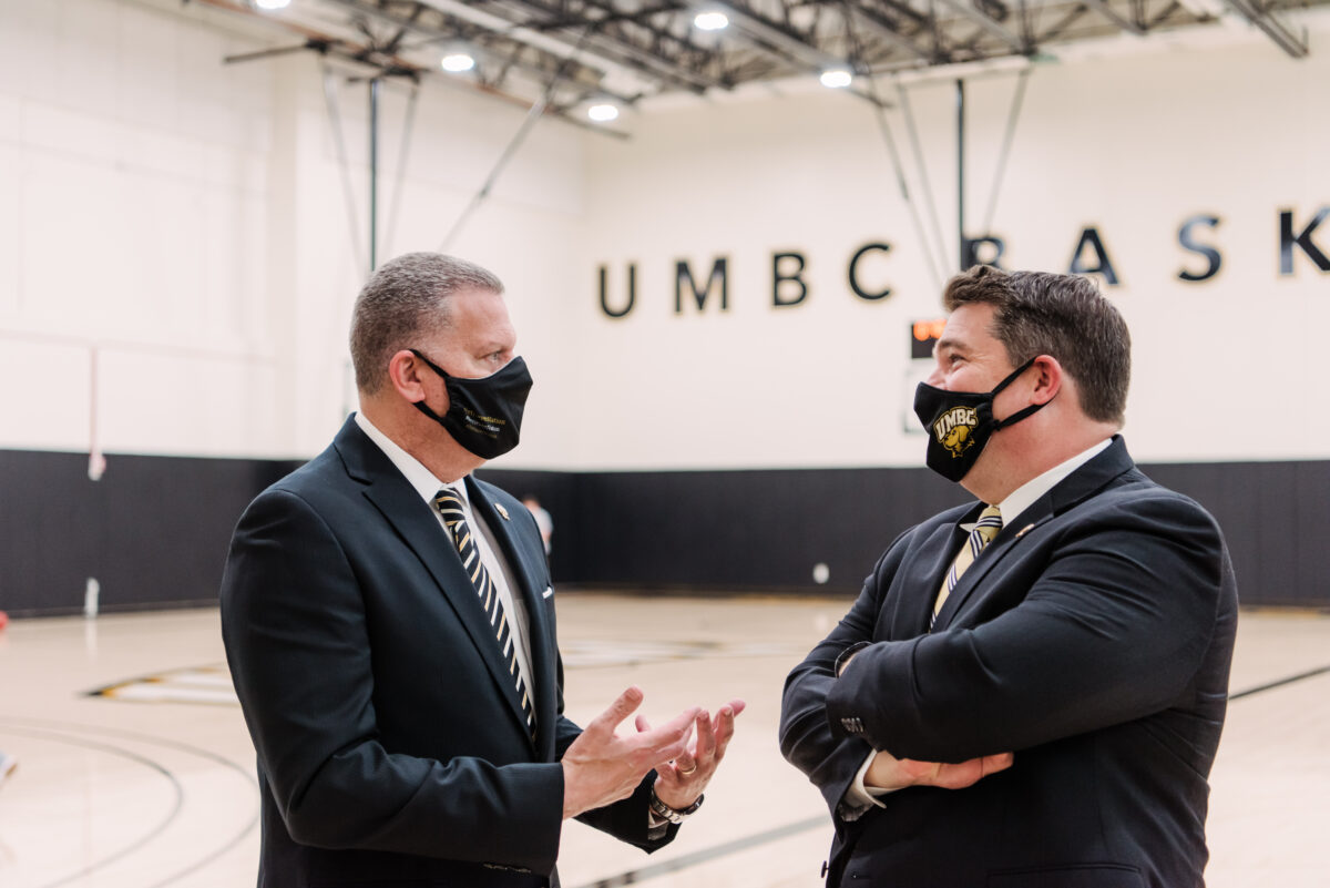 Two men in suits wearing face masks talk on a basketball court