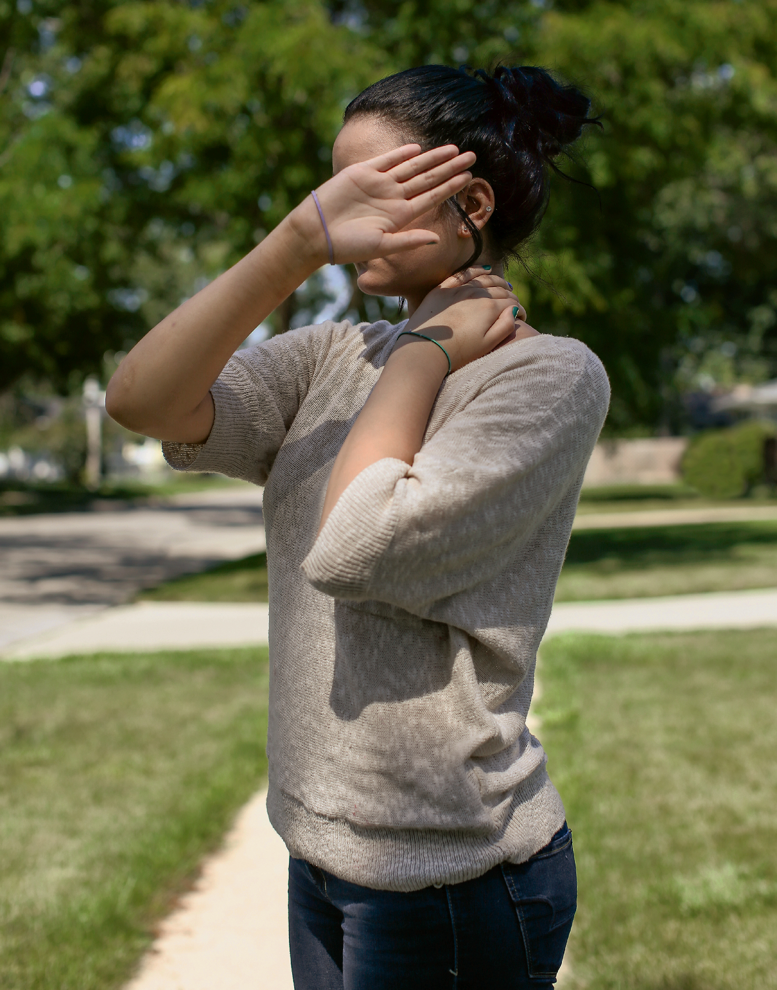 A black woman in a light brown sweater shields her face from the camera