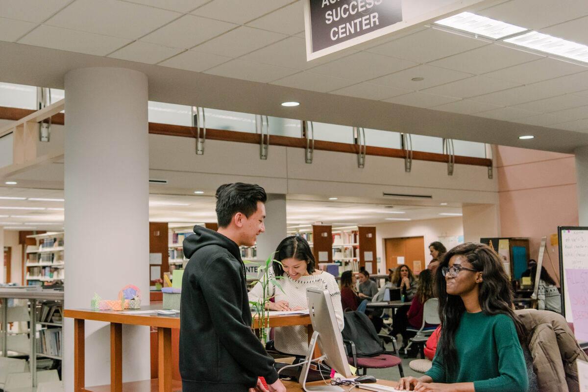 Two students talking at a desk in a library