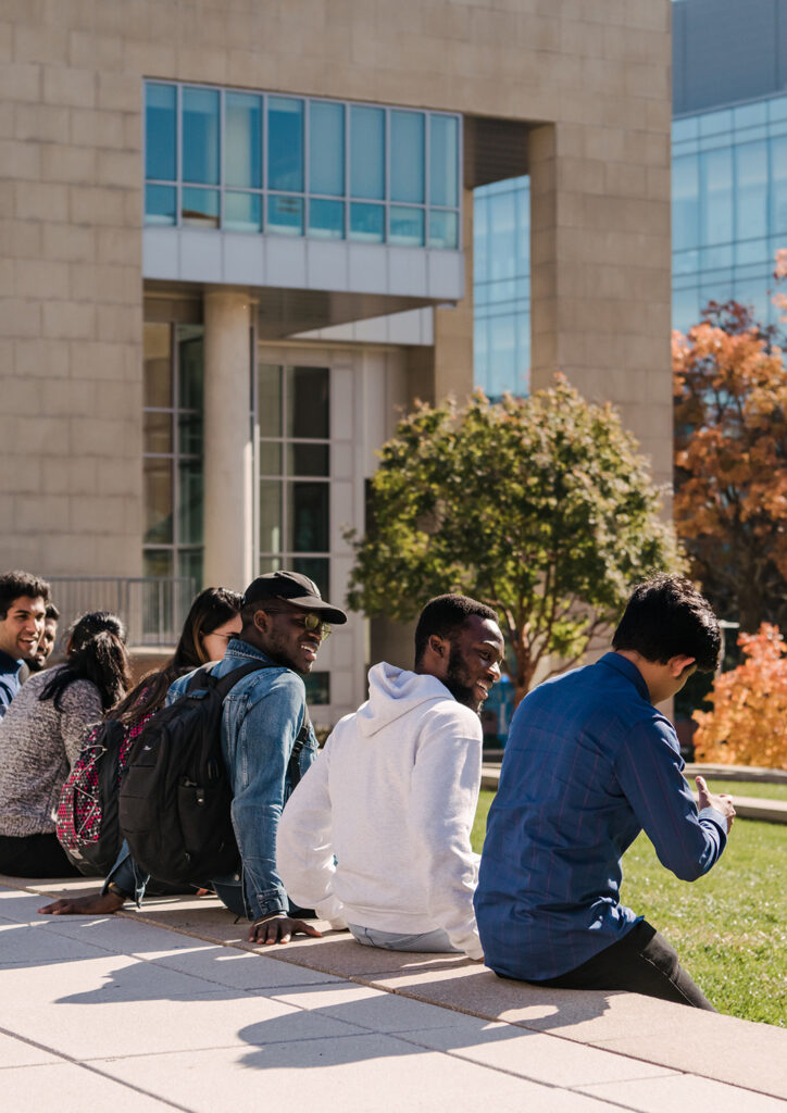 A diverse group of students sit in a row together outside.