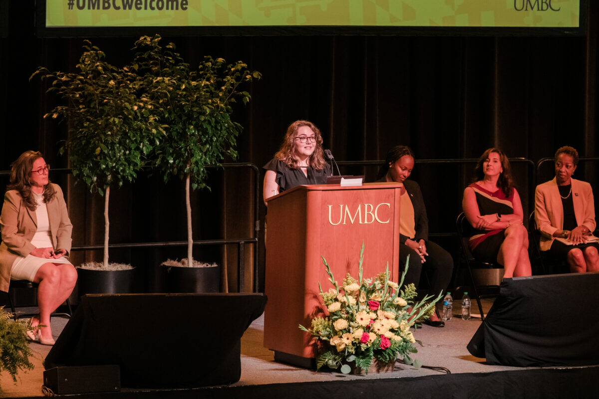 Female student with glasses, from the incoming class, speaking at UMBC podium to start academic year