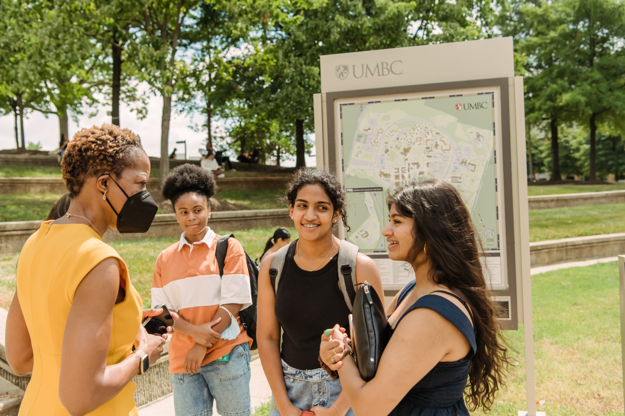 President Sheares Ashby talks with three students outside by a UMBC map