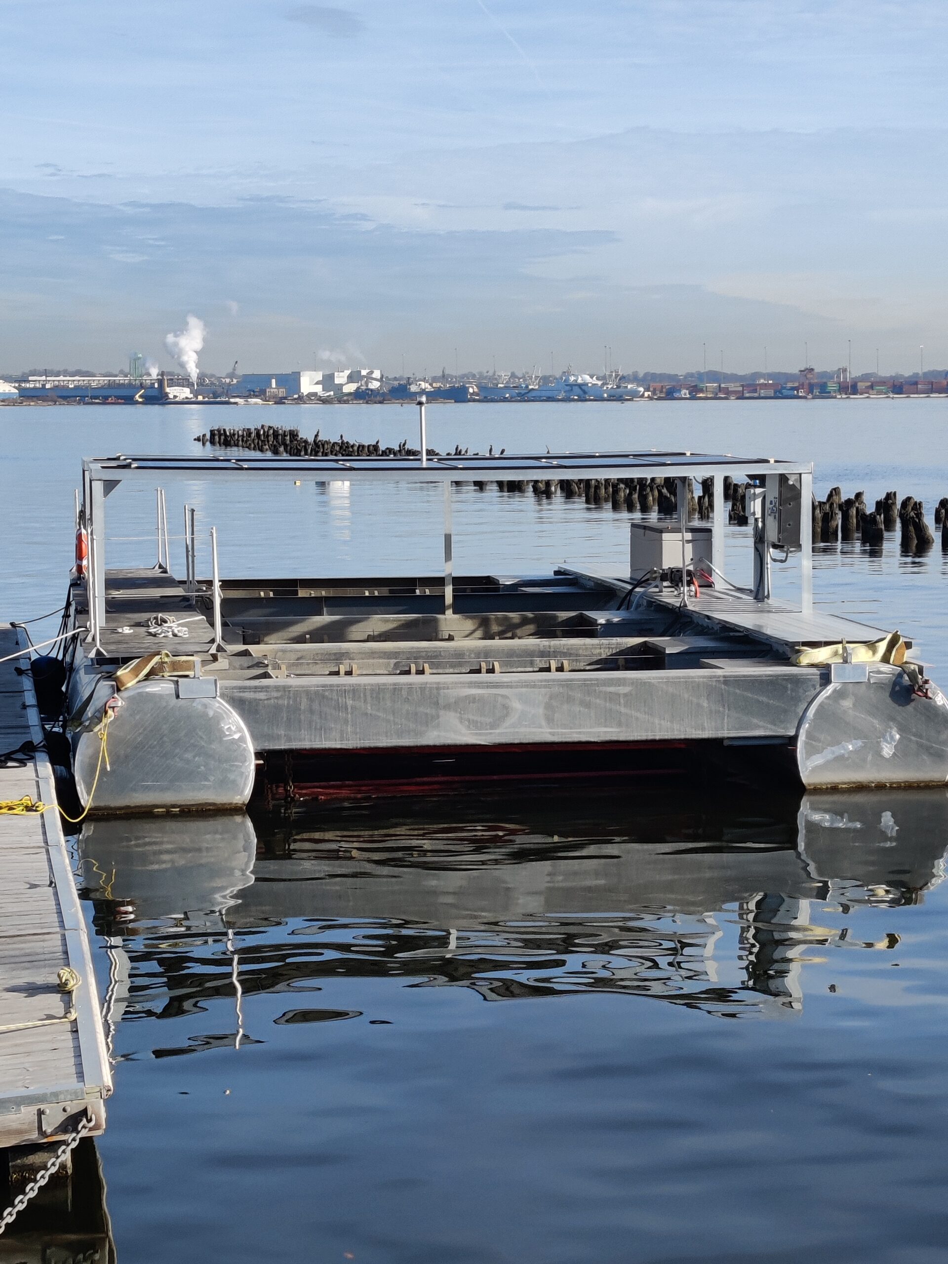 a layer of solar panels above floating oyster baskets, kept afloat by air-filled pontoons and near a dock