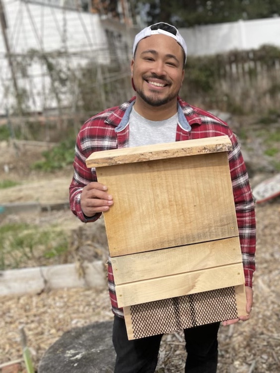 Chris Blume outdoors, holding a wooden bat box about the size of his torso