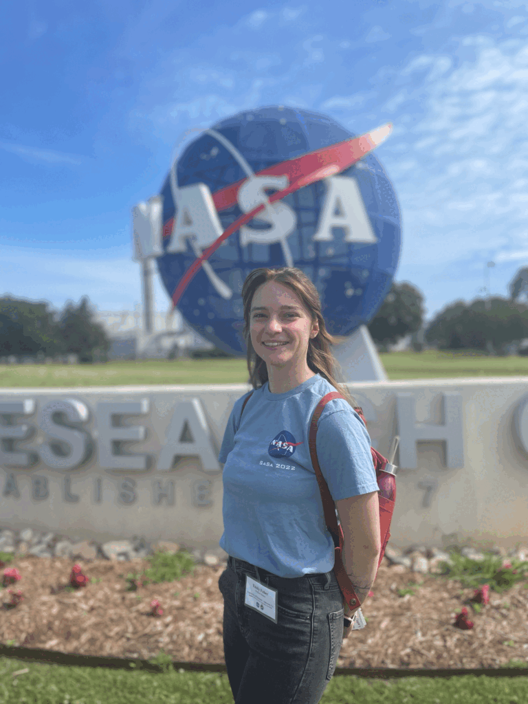 A woman stands in front of a large NASA sign.