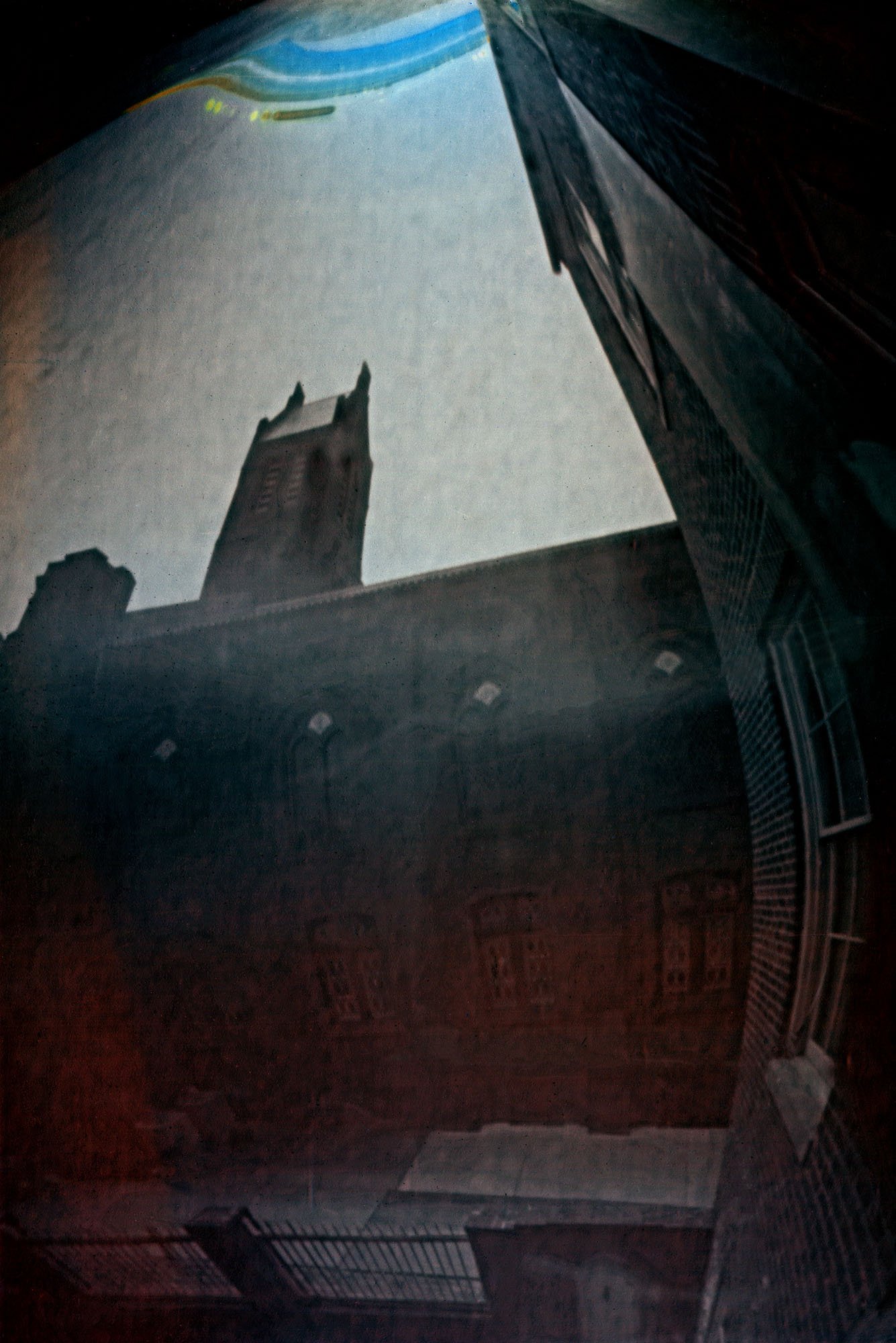 In an image made with a non-standard camera, the top of a chuch is seen against the sky.