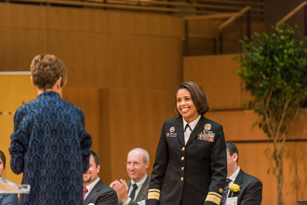 Woman in high-ranking military attire smiles as she approaches a podium