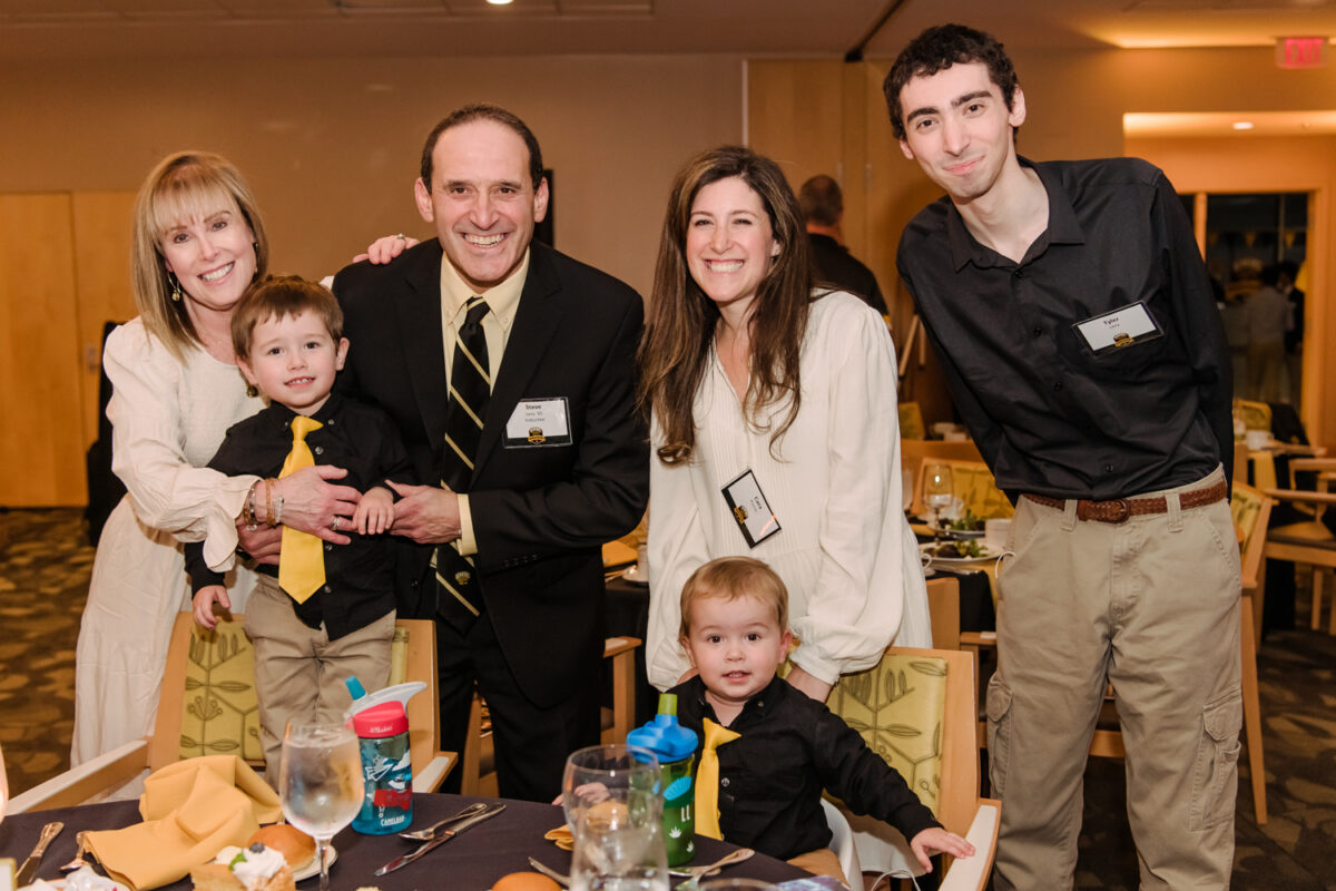 A family dressed in black and white and gold poses together behind a dinner table