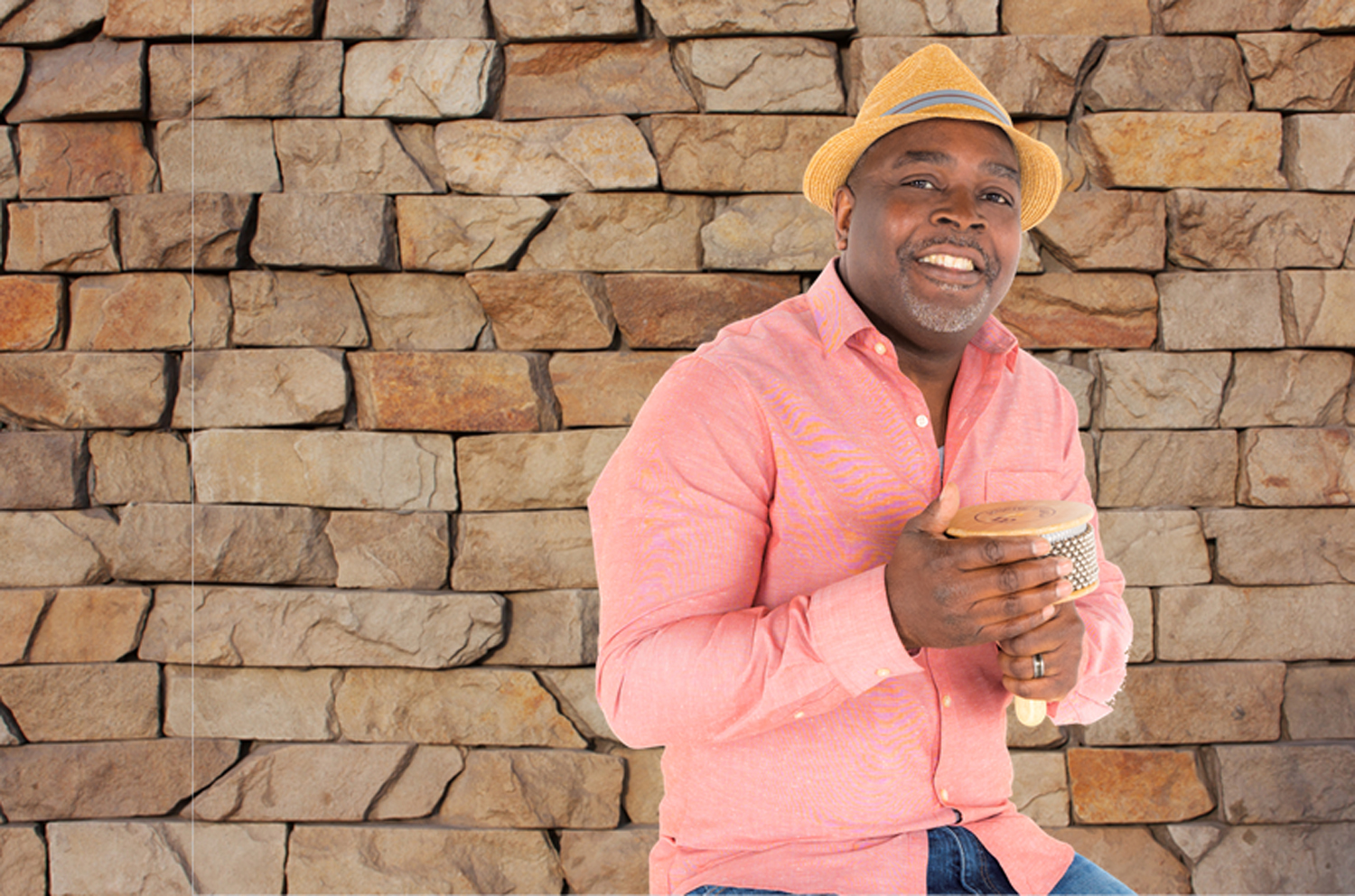 a man in a peach colored shirt and a hat plays a cabasa