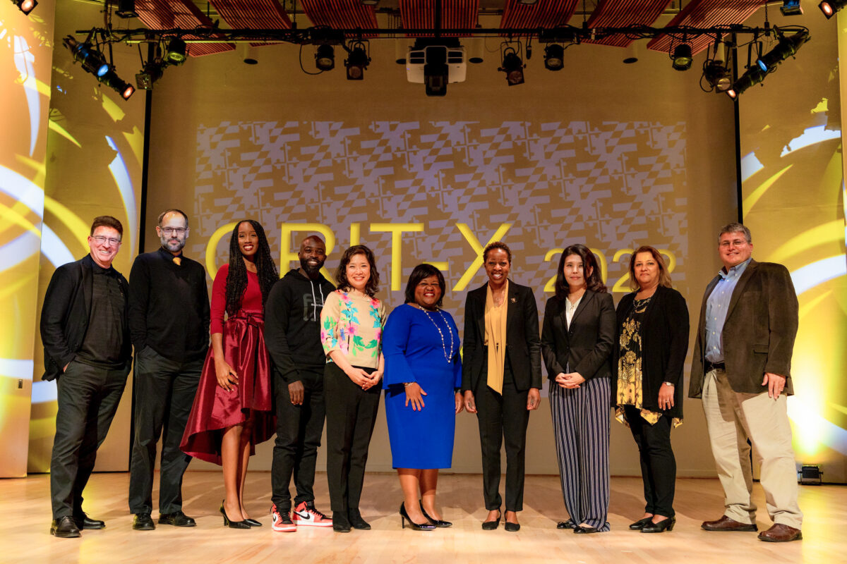 10 people in professional clothing pose, smiling at camera in front of GRIT-X 2022 backdrop.