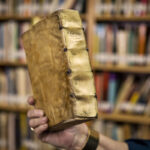 A hand holds an antique book.
