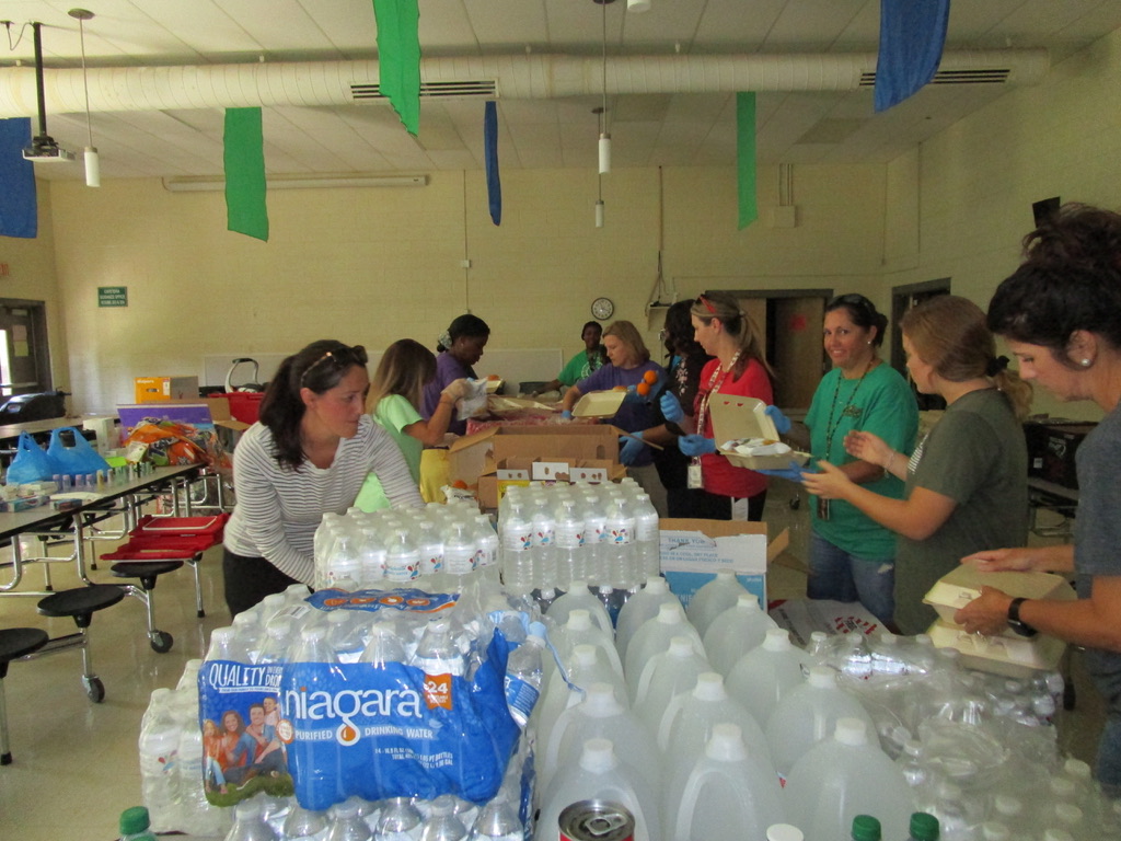 A group of adults organize a bulk food packaging line in a cafeteria.