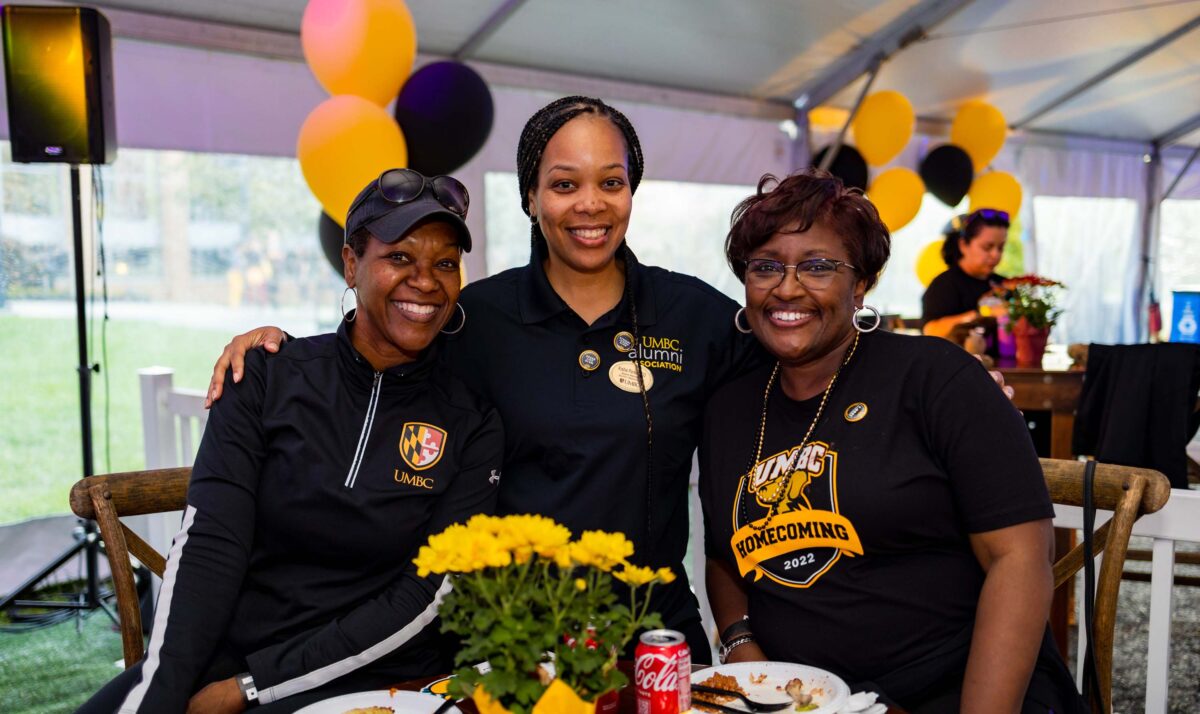 three women in black and gold pose happily behind a table
