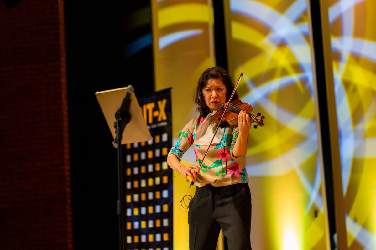 a woman in a flower shirt plays the violin on stage