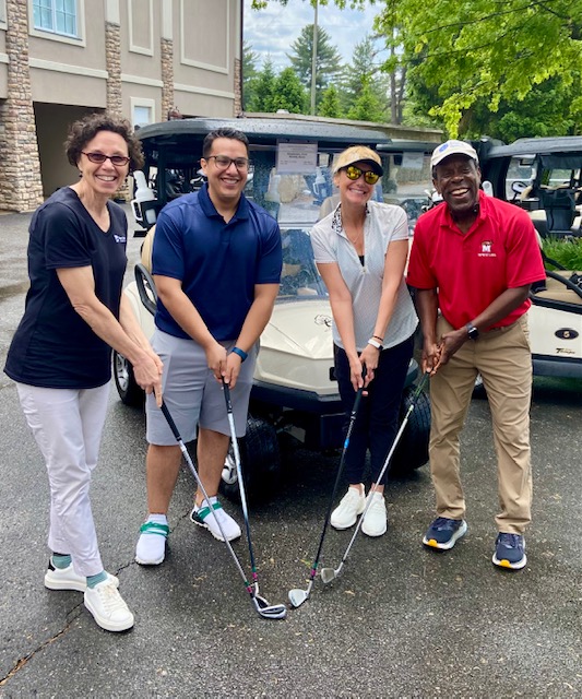 Four smiling people in tennis apparel stand in a semicircle, holding their clubs in front of them.