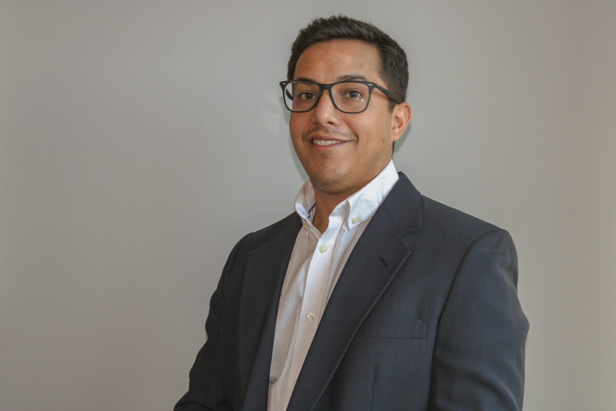 A man wearing glasses and a suit smiles at the camera.