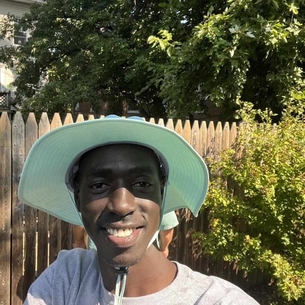 A man's smiling face under a wide brimmed hat. Jok is UMBC's first Peaceworker Global Fellow.