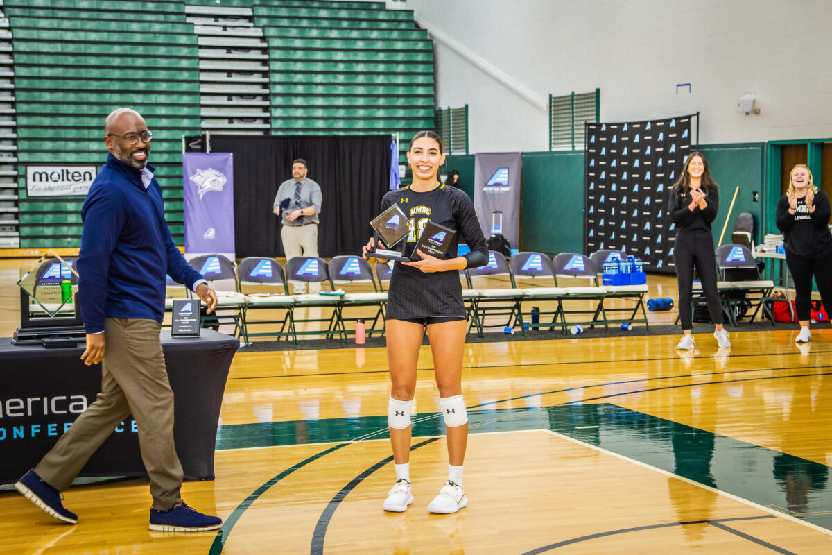 Volleyball player standing on court in uniform holding an award.