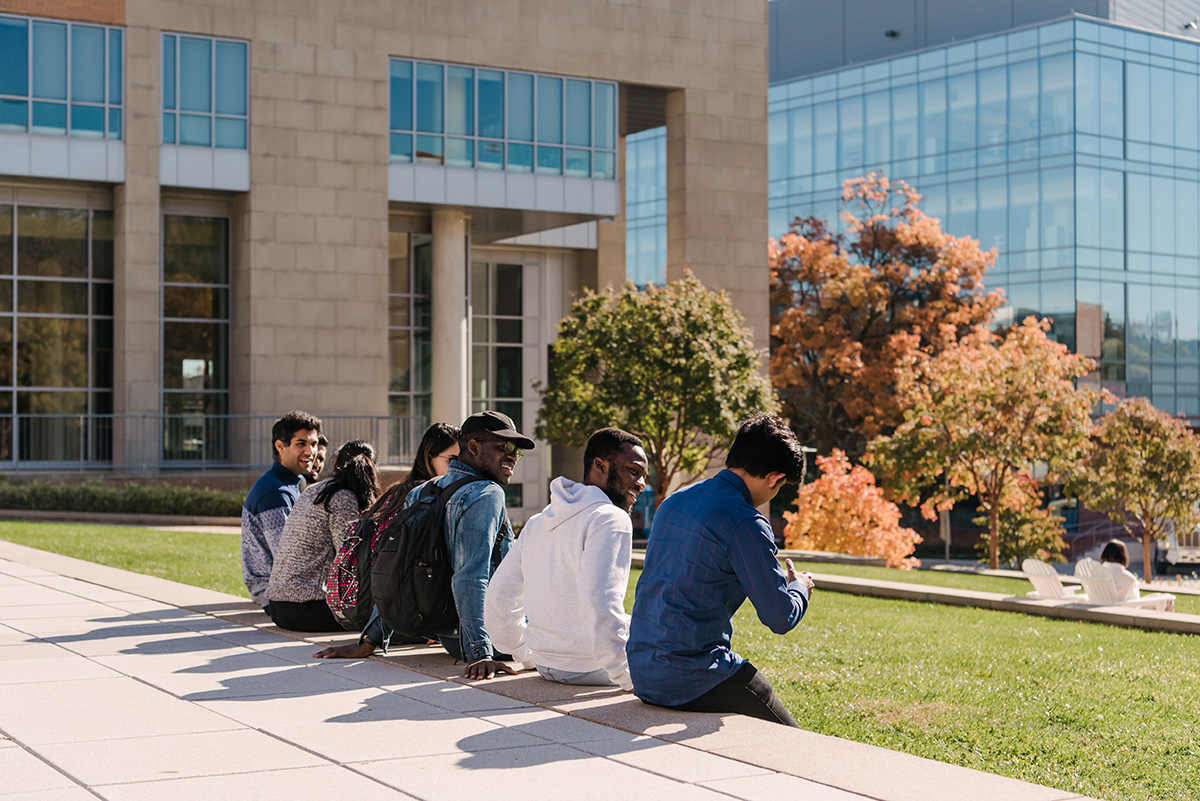 A diverse group of students sitting in a row outside together.